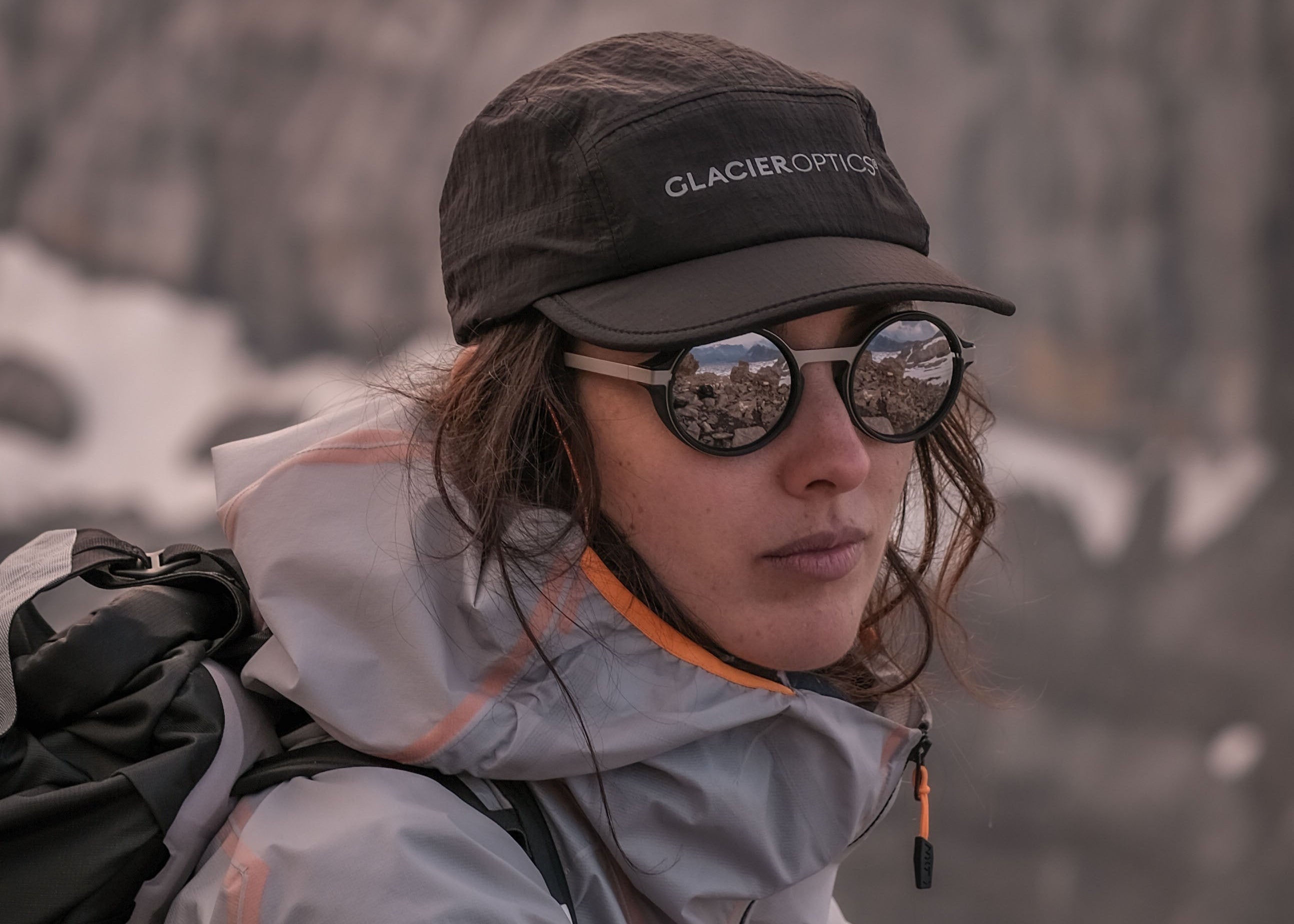 Person wearing a Glacier Explorer cap and sunglasses with a mountainous background