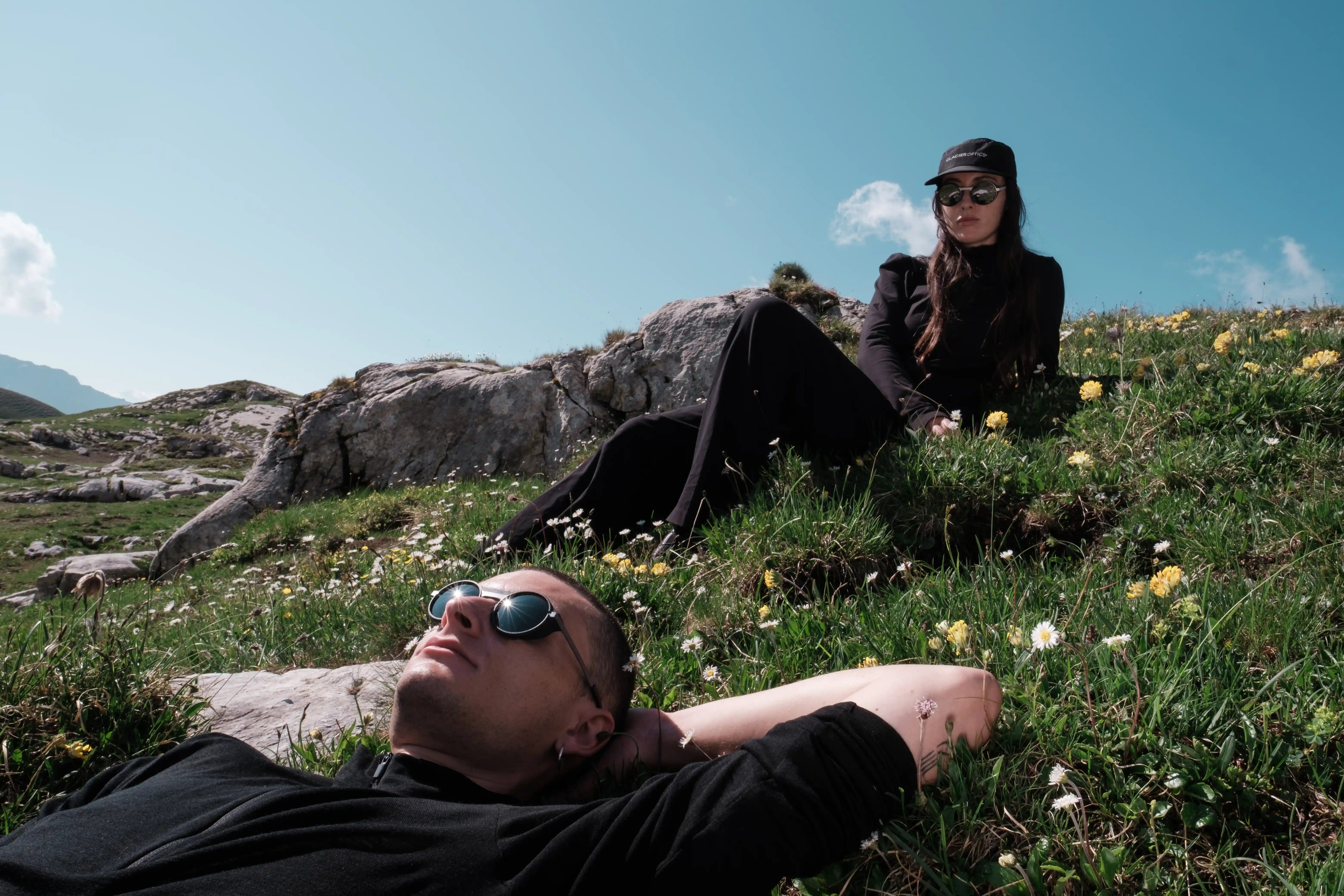 SUNGLASSES MADE IN THE ALPS Young man walking on a snowy mountain with his alpinist and ski materials, snowy mountains and his friend in the background