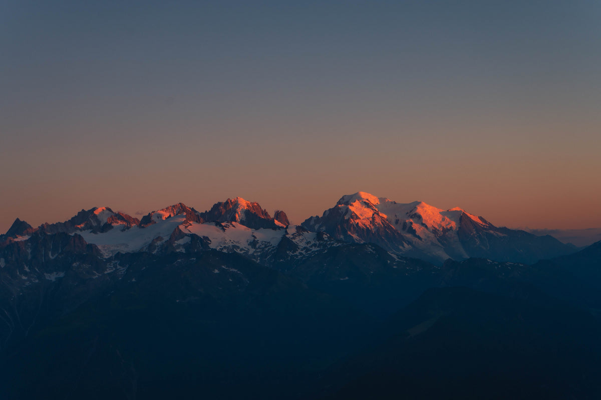 Snow-capped mountain peaks illuminated by warm orange sunset light against a deep blue and orange sky.