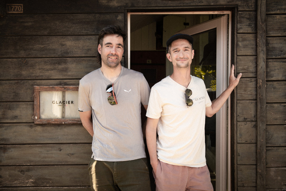 Founders standing in front of a wooden hut with a 'Glacier Optics' sign.