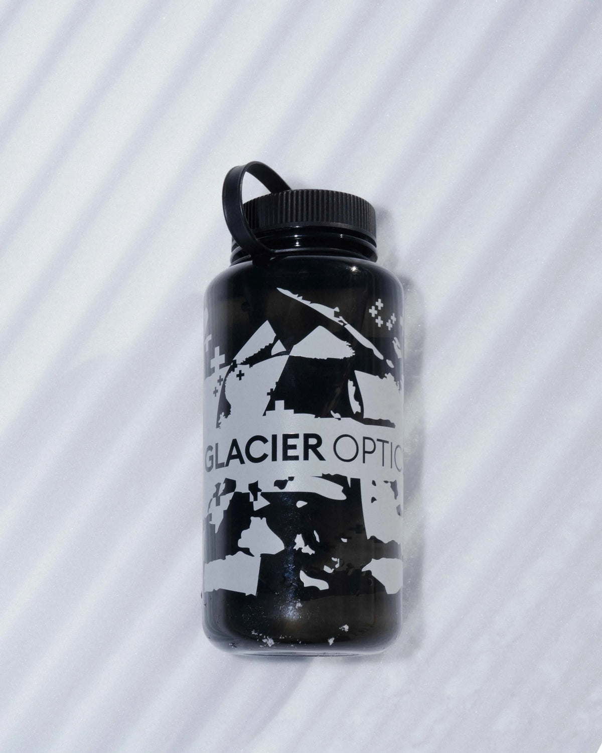 A black plastic water bottle with a black cap and handle, featuring a white graphic of a mountain and the text 'GLACIER OPTICS', set against a white background with diagonal shadows.