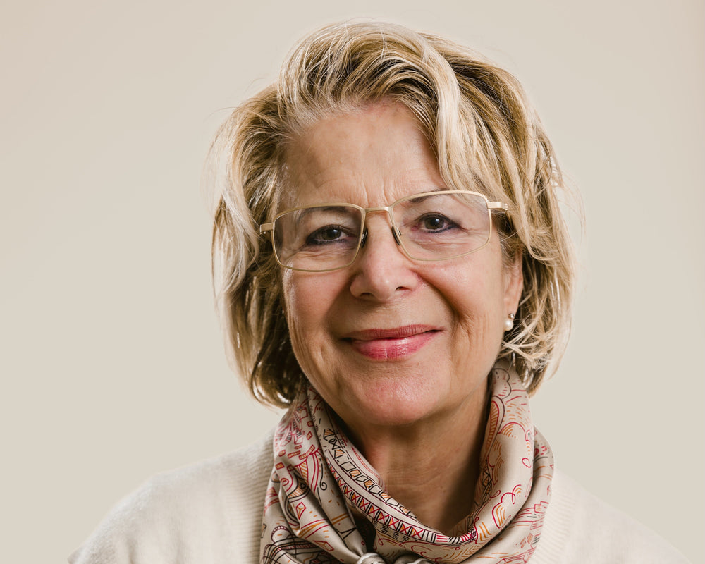 Woman wearing a patterned scarf and glasses against a plain background