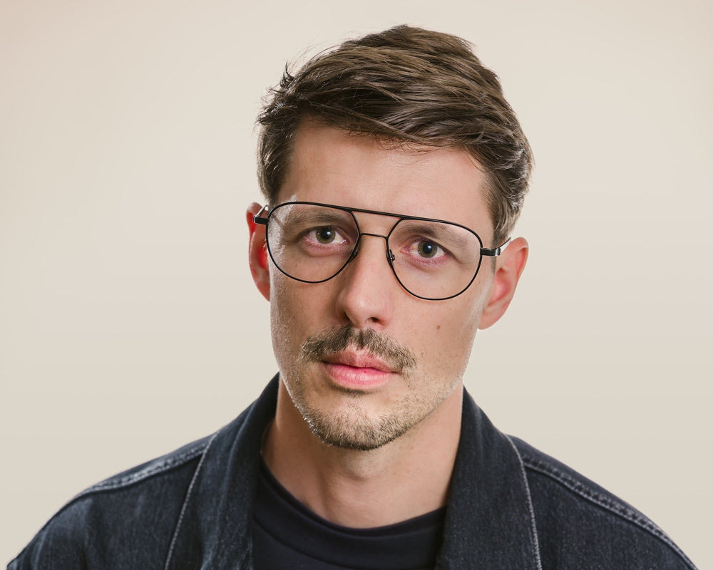 Man wearing glasses and a denim jacket against a plain background