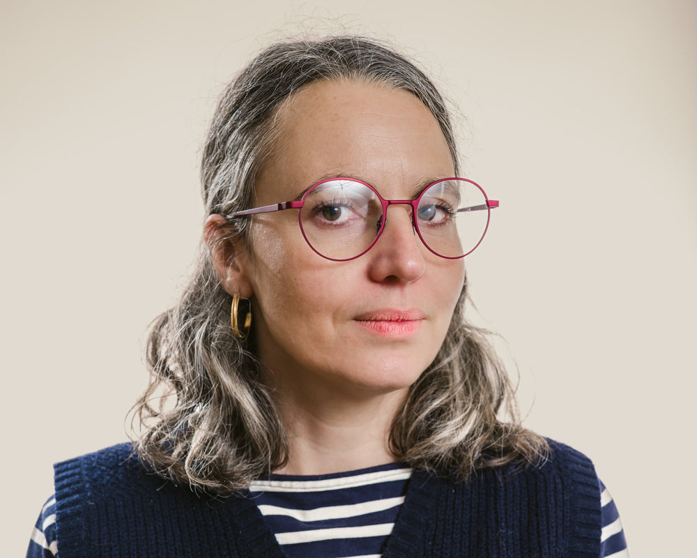 Woman wearing a navy vest over a striped shirt against a beige background