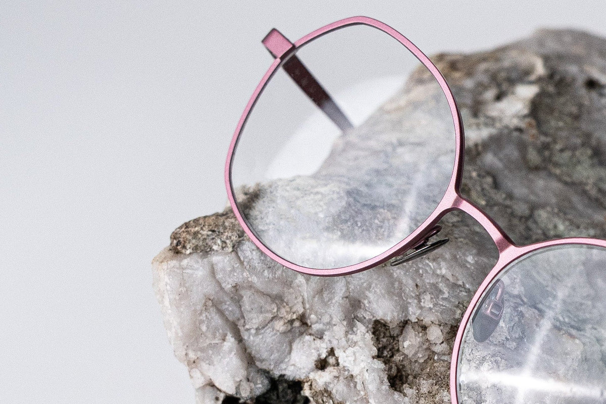 Pink butterfly cut titanium eyeglasses on a textured rock surface