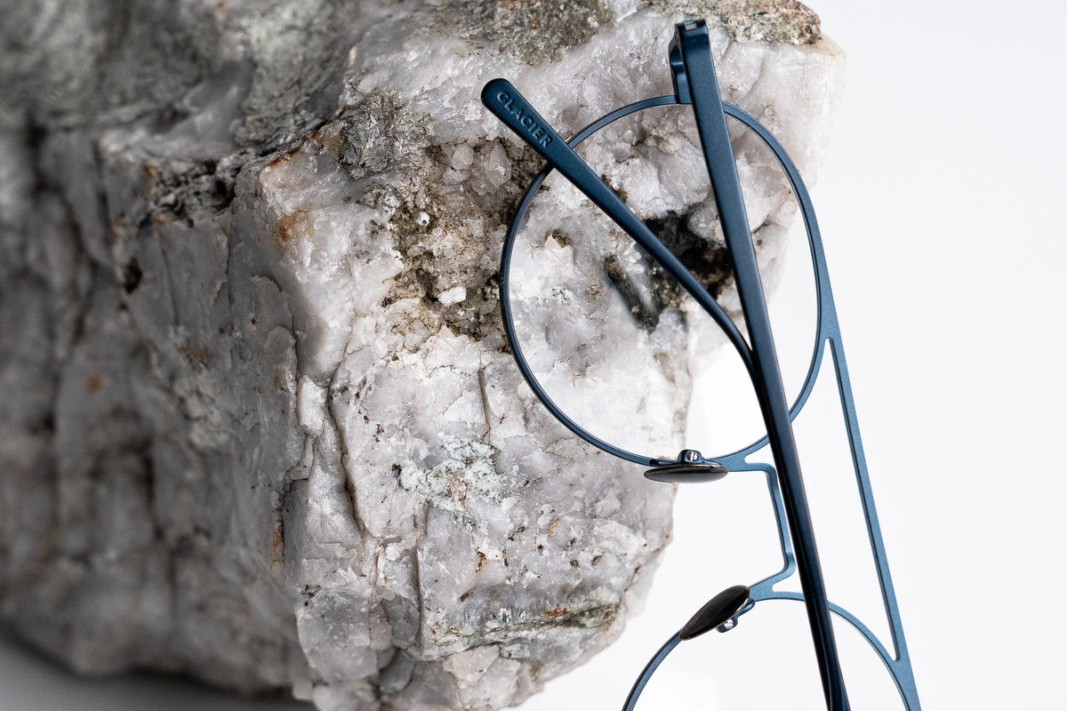 Blue titanium eyeglasses on a white surface with an alpine rock formation in the background