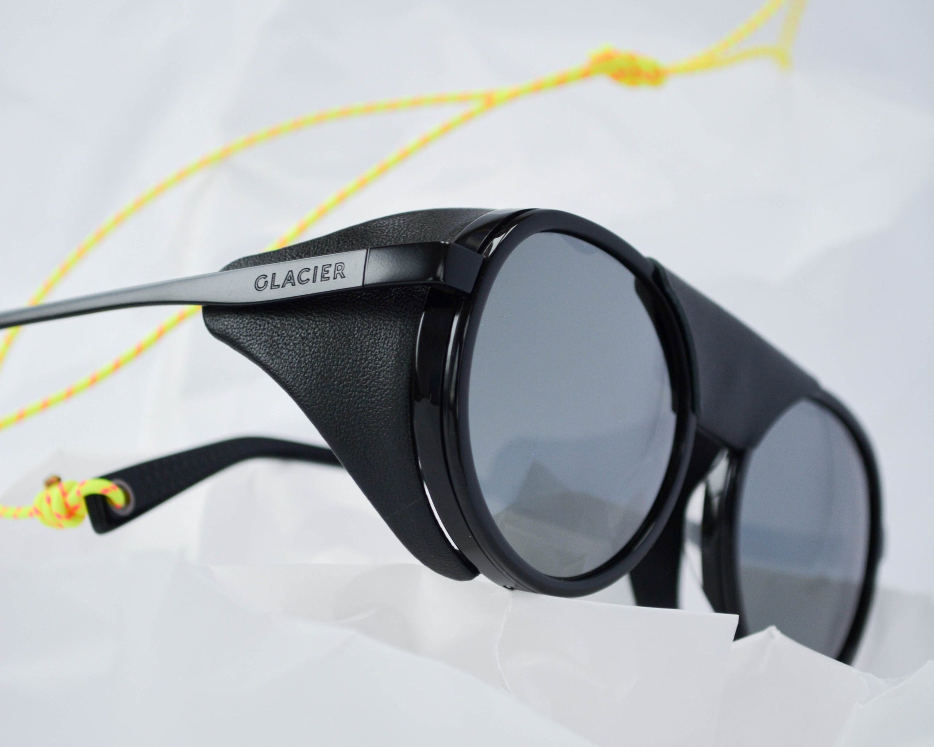 Black titanium and acetate moiry sunglasses with a yellow upcycled paragliding string on a white background