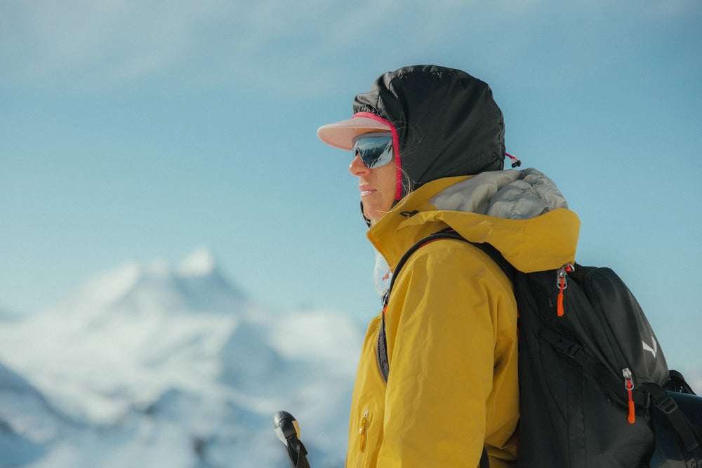 A person in a Pierredar grey sunglasses stands in profile against a snowy alpine mountain and blue sky.