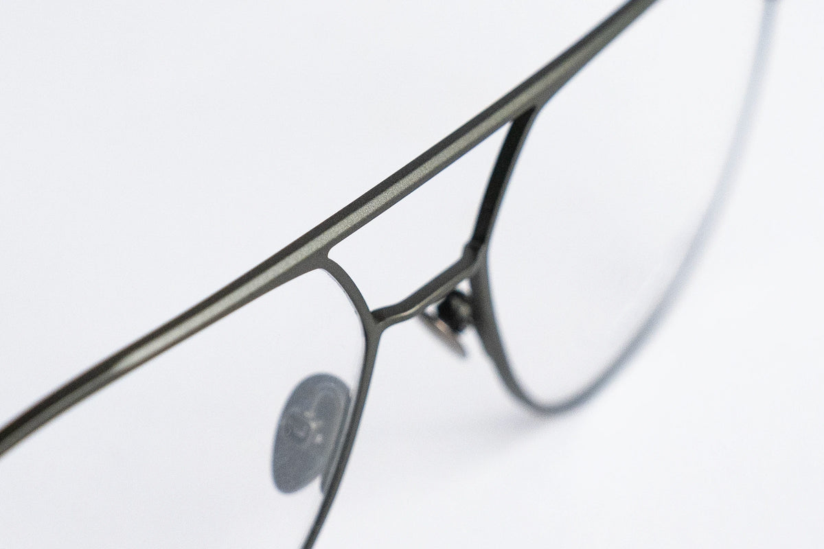 Close-up of an olive-colored avitaior titanium eyeglass frame on a light gray background