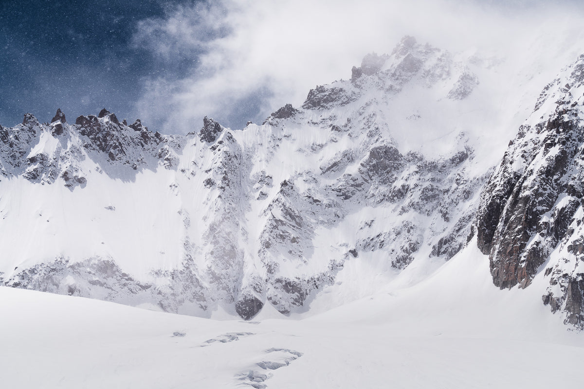 Snow-covered mountain peaks and rocky ridges under a dark blue sky with white clouds.