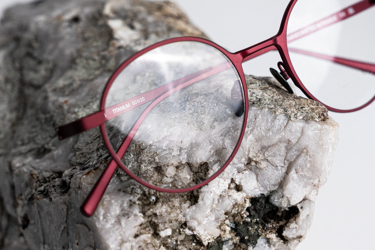 Burgandy-framed titanium eyeglasses on a textured rock surface
