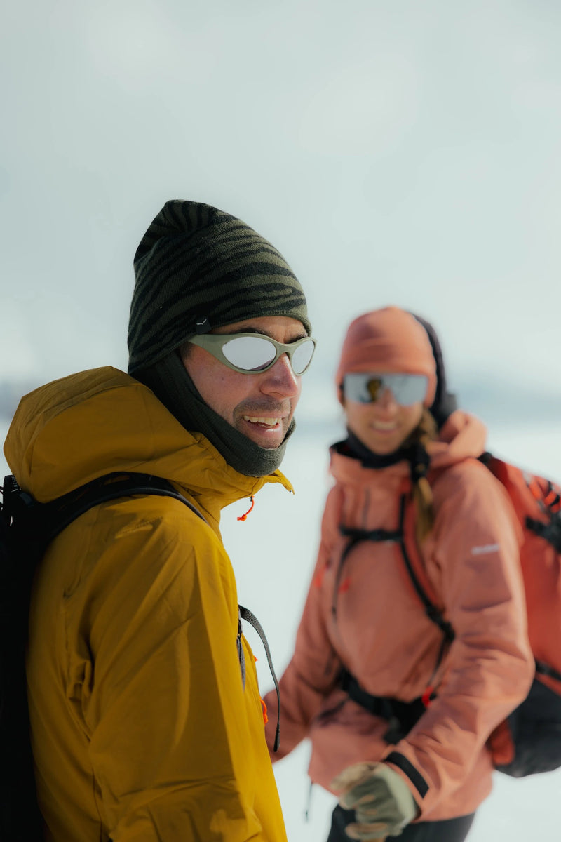 Two people outdoors in winter clothing, with the foreground person wearing a Vorab in olive color, and the background person wearing a Pierredar in grey color.