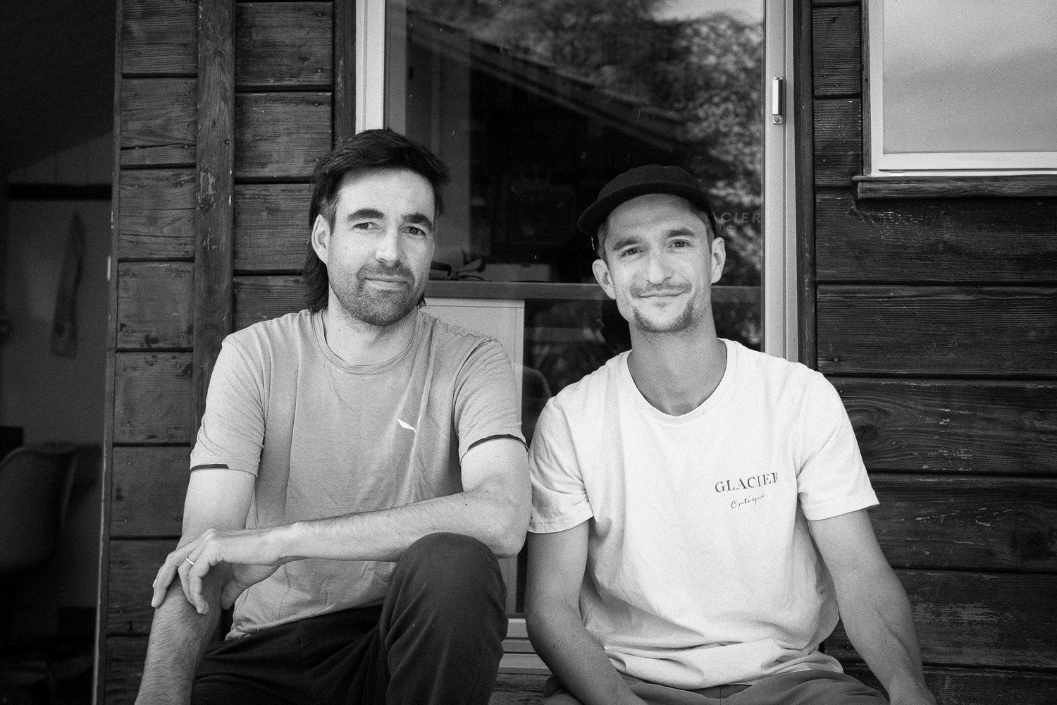 The two founders of Glacier optic in front of a wooden cabin.