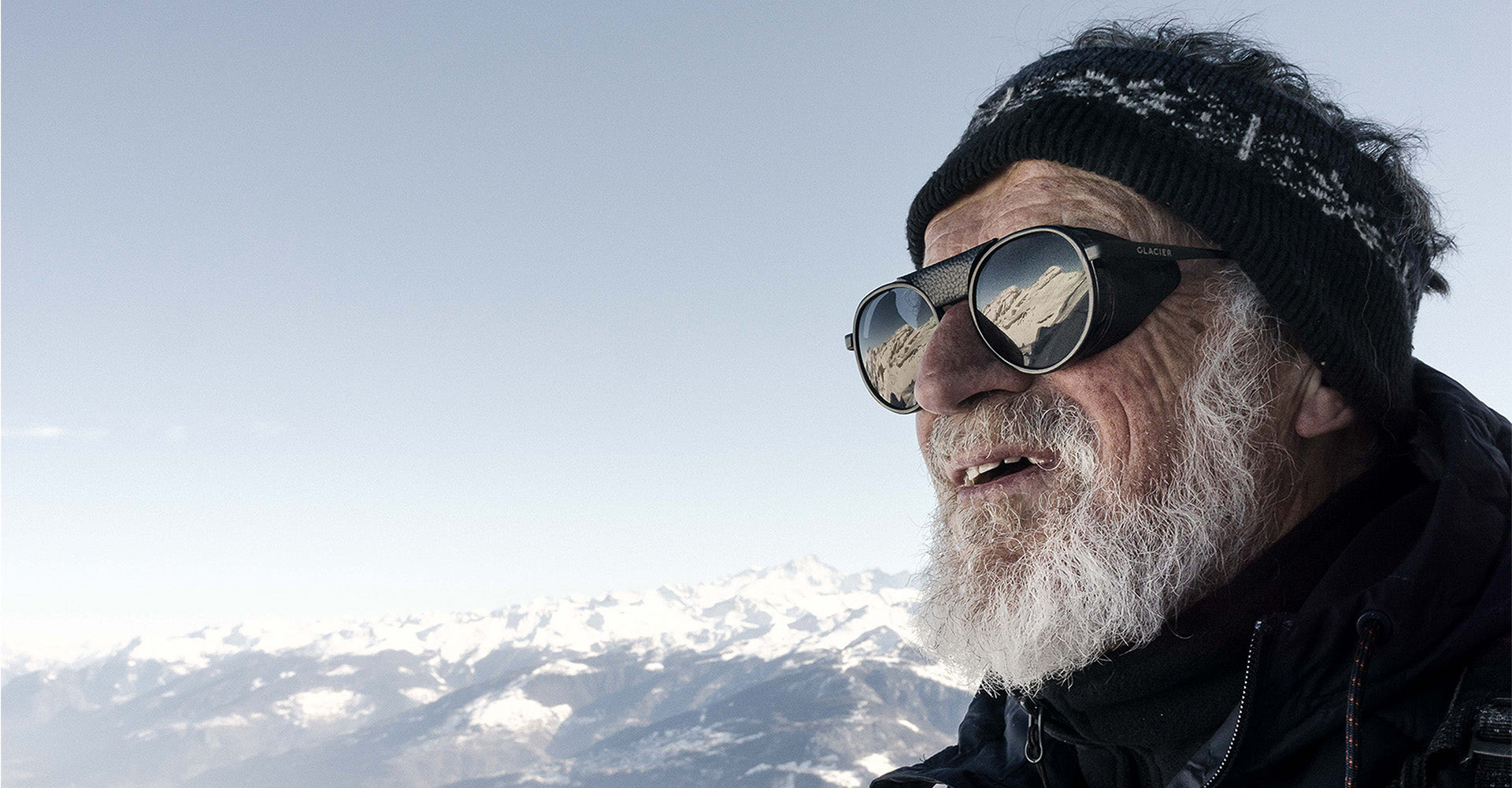 Old man with Glacier sunglasses looking away with snowy mountains in the background